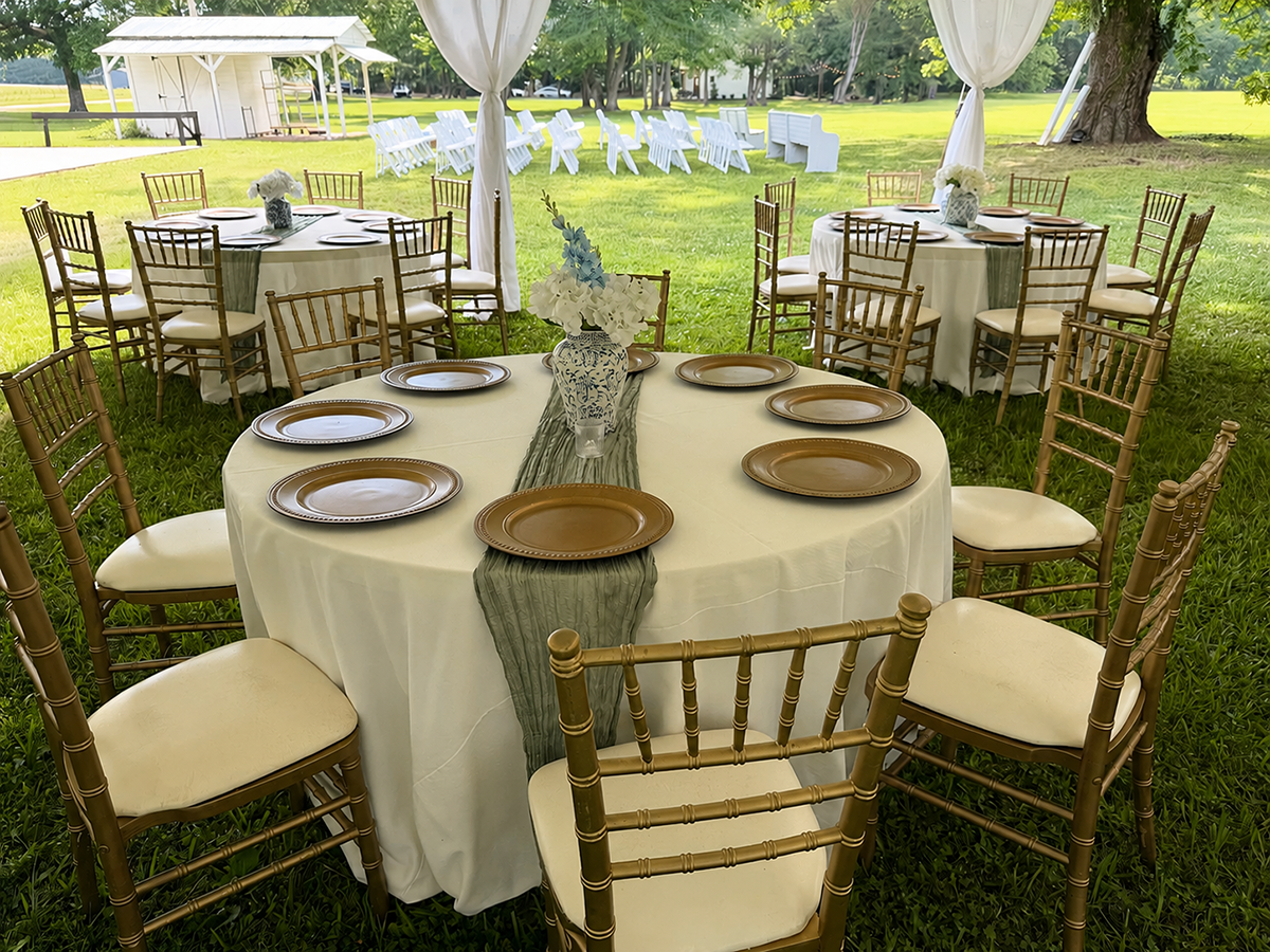Elegant tables, tableclothes, plates, and dining area set up under a tent for weddings.